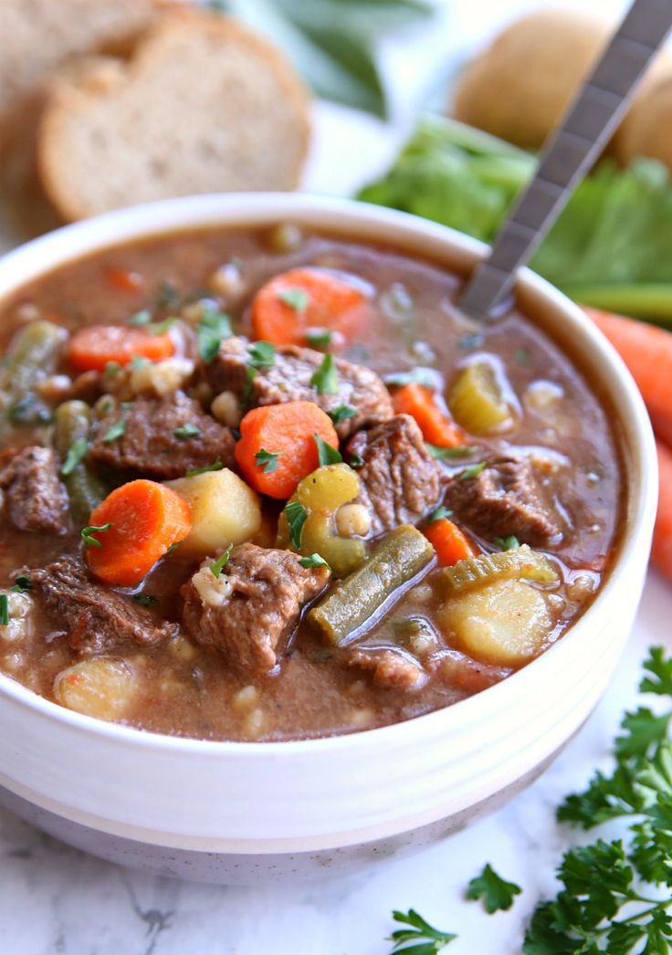 a bowl of beef stew with carrots, celery and bread on the side