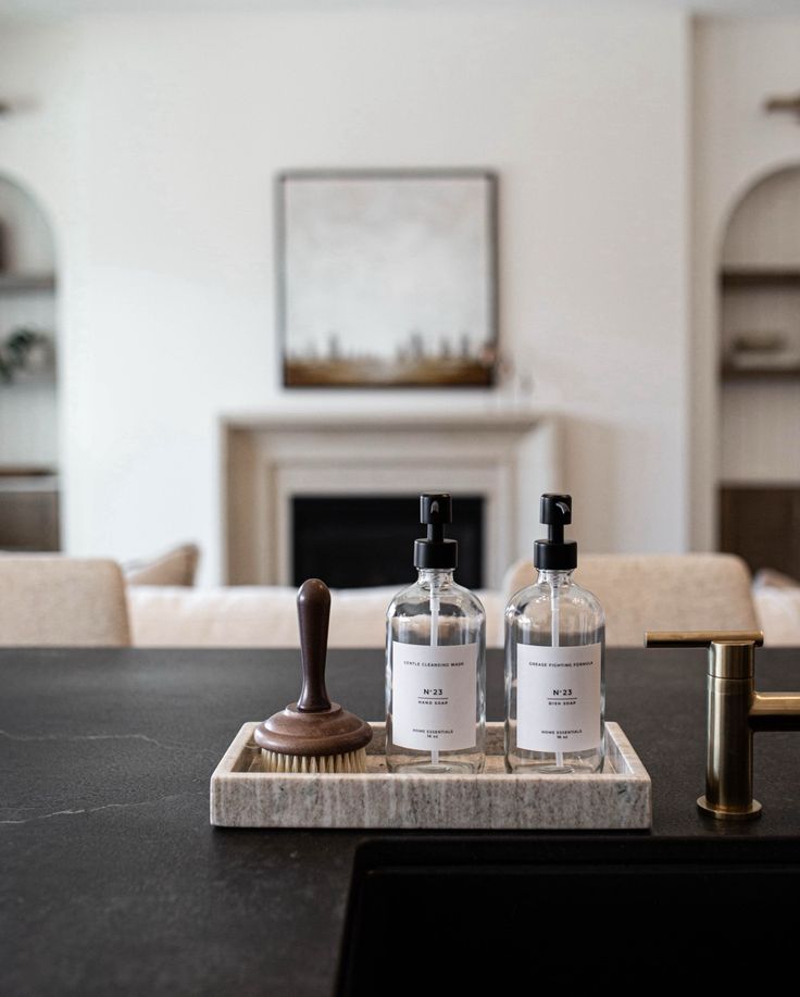 two bottles of alcohol sitting on top of a wooden tray next to a brush and soap dispenser