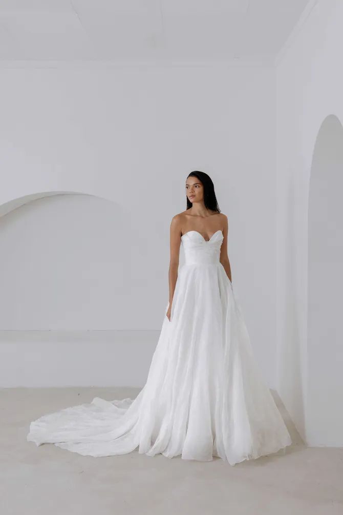 a woman in a white wedding dress standing next to a wall and looking at the camera