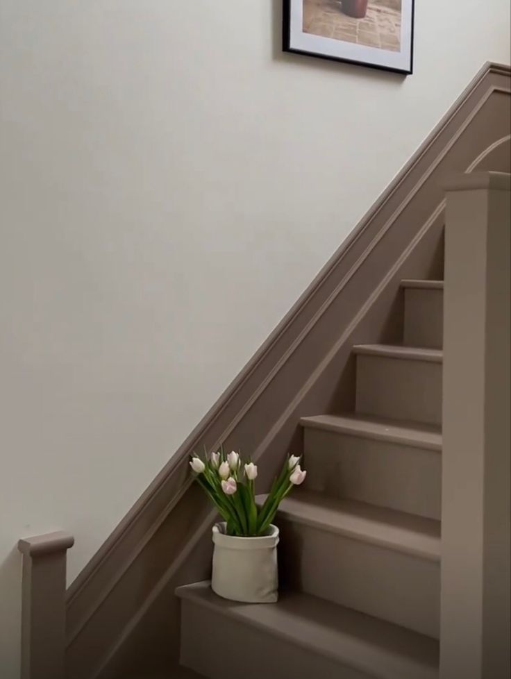 a vase with flowers sitting on the bottom of some stairs next to a framed photo