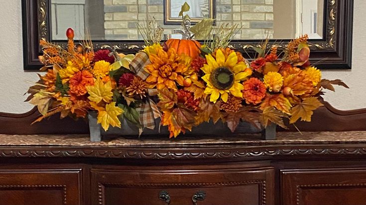 a wooden dresser topped with lots of flowers and fall leaves in front of a mirror