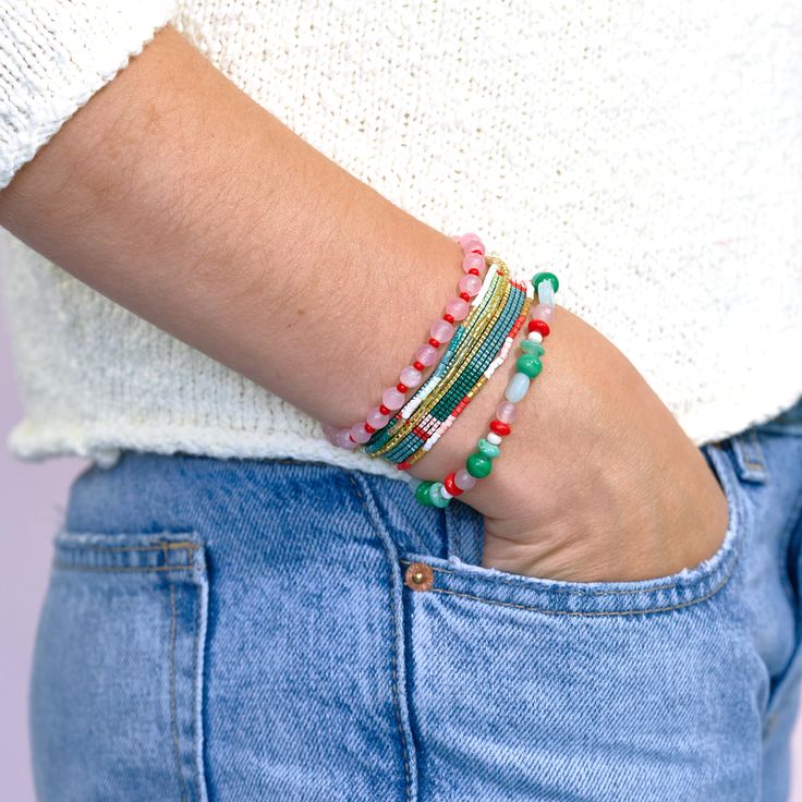 Embrace bohemian chic with our Mixed Bracelet Stack of 6 Fields of Poppy. This vibrant set features an enchanting mix of red, green, and gold seed beads. The varied textures and patterns of the beaded strands create captivating visual interest. Stretchy elastic cord ensures a comfortable fit for most wrists. Lightweight and easy to wear, this bracelet stack is perfect for adding a pop of color to your everyday look or elevating a special outfit. Individual bracelet strands may vary slightly. Packaged on our signature bracelet card. --DETAILS-- Handmade by skilled artisans in India Hypoallergenic nickel + lead-free brass hardware These accessories are made by human hands. A slight variation in size and color is considered part of the beauty of these one-of-a-kind pieces. To extend the life Green Wrap Bracelet With Round Beads For Festival, Multicolor Friendship Bracelets With Gold Beads For Beach, Multicolor Gold Beads Friendship Bracelet For Beach, Green Bohemian Stretch Bracelet With Faceted Beads, Green Multi-strand Wrap Bracelet As Gift, Bohemian Festive Bracelets With Faceted Beads, Green Beaded Wrap Bracelet For Festival, Bohemian Bracelets With Faceted Heishi Beads, Festive Green Beaded Bracelets With Colorful Beads