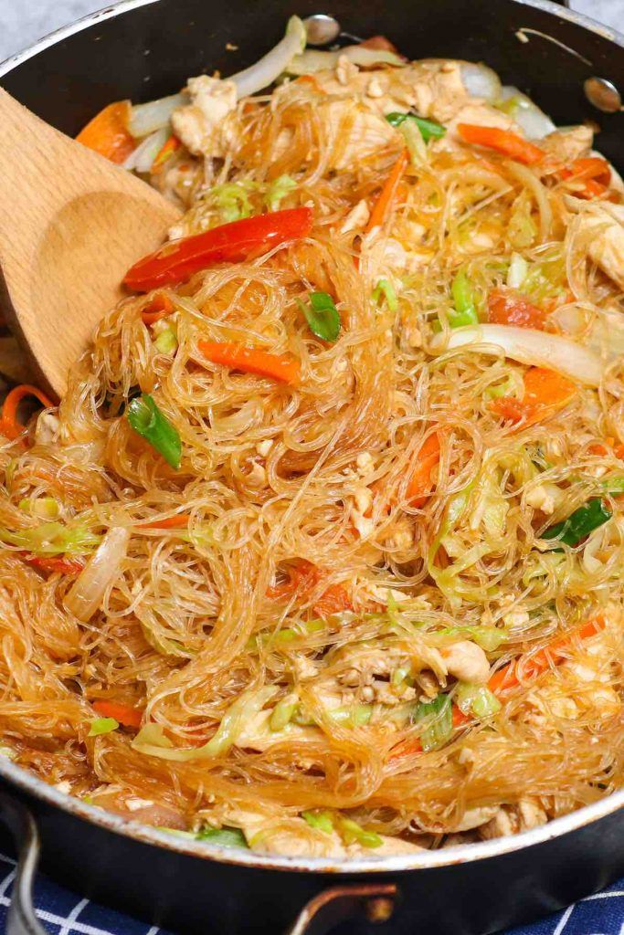 a wok filled with noodles and vegetables on top of a blue checkered table cloth