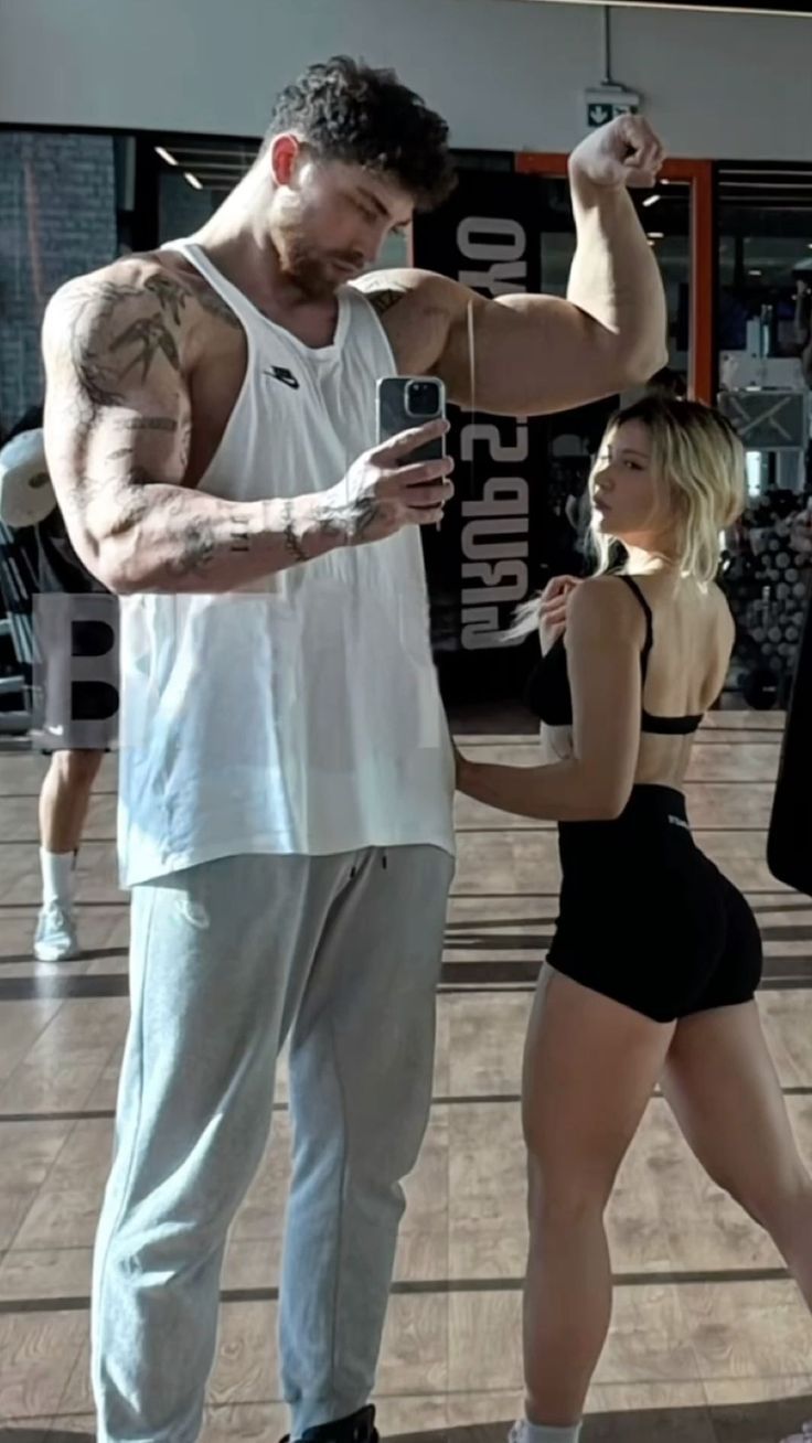 a man standing next to a woman on top of a hard wood floor holding a cell phone