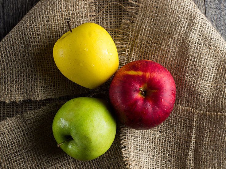 two apples and one yellow apple on a burlap cloth