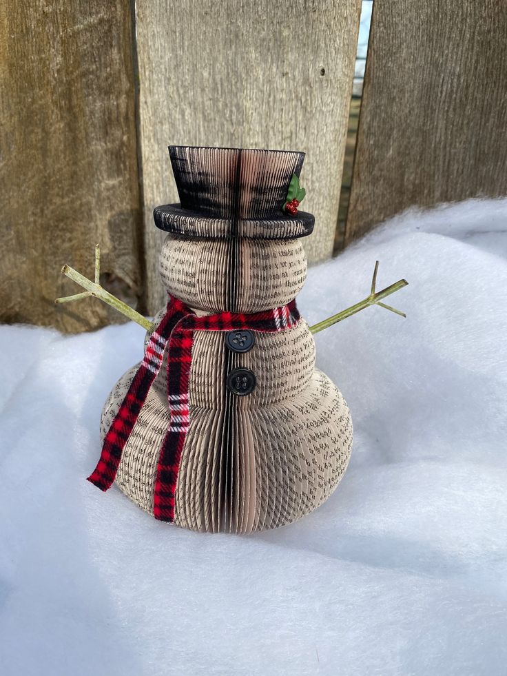 This Snowman is made from damaged or used paper back books.  Measures 7 inches tall and is made with real wooden arms, plaid scarf, black buttons, and a holly leaf on his hat.  If you would like any customization, please message me and I would be glad to help. Recycled Book Crafts, Upcycled Books Crafts, Winter Whimsy, Book Club Gifts, Book Page Roses, Advent Crafts, Christmas Booth, Old Book Crafts, Christmas Decorations Centerpiece