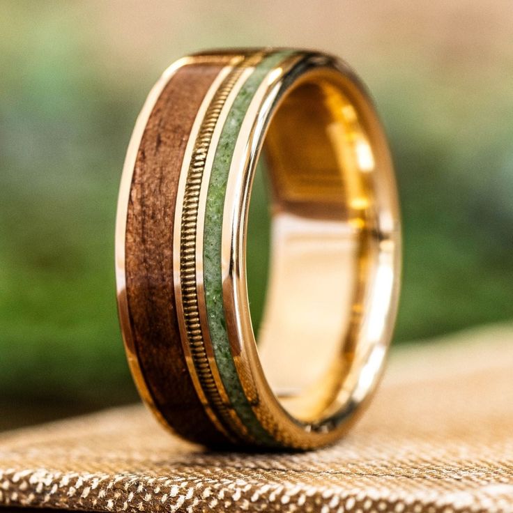 a gold ring with green and brown wood inlays sits on top of a wooden table