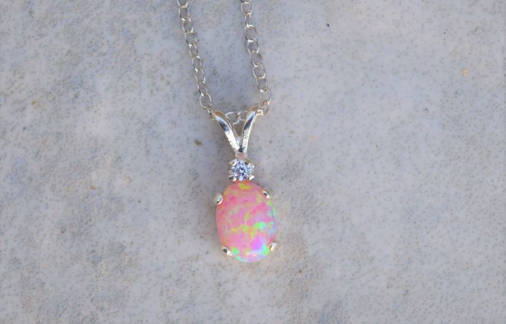 "Gorgeous pairing of a pink opal and CZ accent gemstone. The gemstones are handset into a sterling silver pendant and hung from a sterling silver chain. This pink opal has amazing flashes of color when it catches the light. The resulting necklace is stunning yet simple, a truly elegant necklace! The necklace ships in a lovely gift box ready to give as a gift or keep for yourself! Pictured with cubic zirconia accent stone color: \"White / Clear - April\" Setting Material - 925 Sterling Silver Cha Elegant Silver Pink Opal Necklaces, Elegant Silver Pink Opal Necklace, Pink Opal Jewelry For Gift, Opal Jewelry With Stones For Gift, Opal Jewelry With Stones As A Gift, Pink Opal Jewelry With Gemstone Detail, Pink Opal Jewelry With Gemstone, Oval Pink Opal Jewelry Gift, Oval Pink Opal Jewelry For Gifts