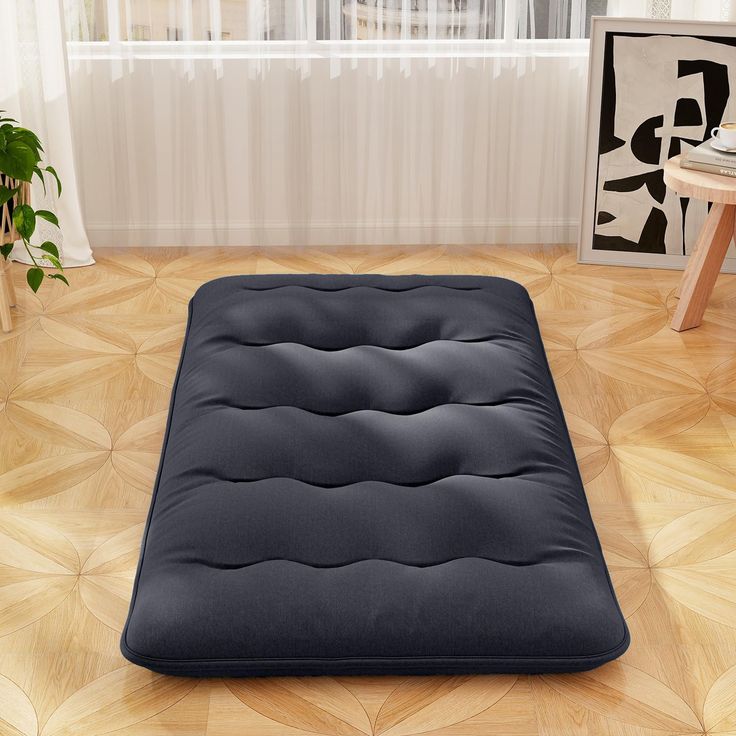 a black futon mattress sitting on top of a wooden floor next to a window