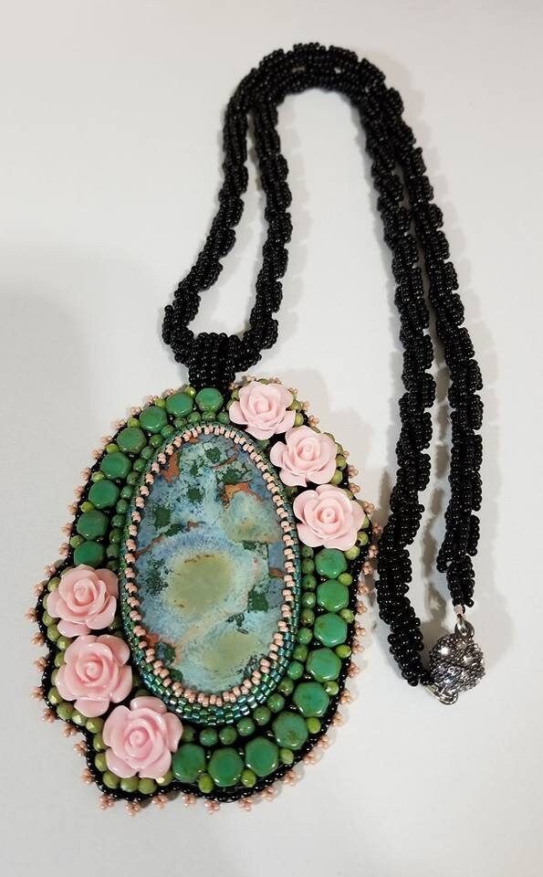 a beaded necklace with flowers and a green oval pendant hangs from a black cord