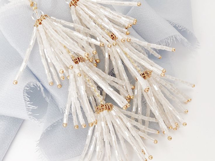 "NEW & WE ARE IN LOVE with these chic hand-beaded tassel wedding earrings, perfect for the boho bride at heart and a fun accessory to wear after the wedding too! Each piece is made in the USA. DETAILS *As shown, earrings feature soft white hand beaded tassels *The earrings measure about 4\" top to bottom and about 1\" wide *Finish is available in gold as shown The goal of your earrings is to compliment your dress and your overall wedding day look, not overpower it. We want our earrings to ma Elegant Tassel Earrings For Festive Occasions, Gold Tassel Earrings For Wedding, Glamorous Gold Tassel Earrings For Wedding, Dangling Beads Bridal Earrings For Wedding, Wedding Bridal Earrings With Dangling Beads, Wedding Bridal Dangle Earrings With Beads, Elegant Beaded Chandelier Earrings For Festive Occasions, Silver Tassel Wedding Earrings, Pearl White Beaded Earrings For Wedding