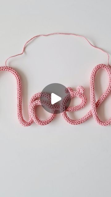 the word noel spelled out in pink yarn with a grey circle around it and an arrow