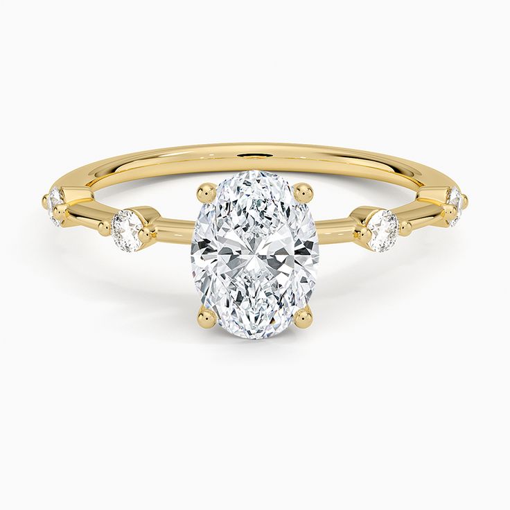 an oval cut diamond ring with three stones on the band and shoulders, set in yellow gold