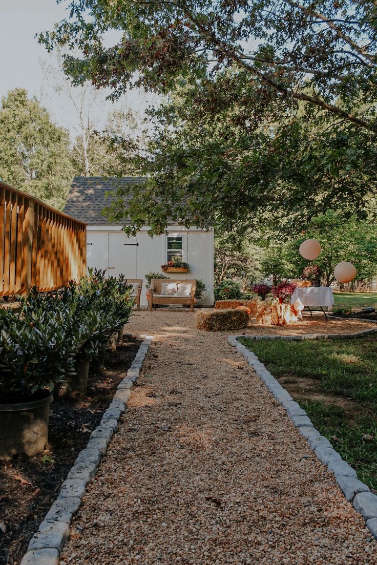 a gravel path leading to a small white house in the distance, with tables and chairs set up on either side