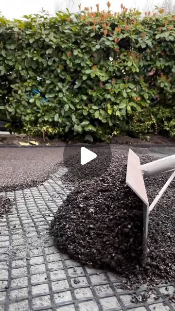 a white metal object sitting on top of a pile of black gravel next to a green hedge