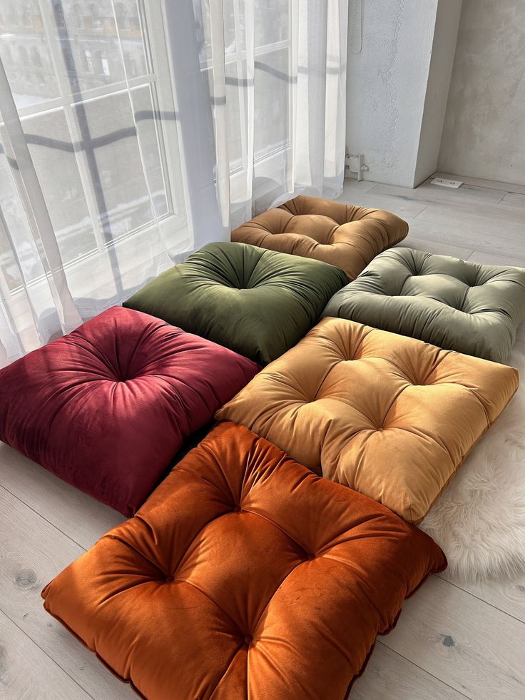 four different colors of square cushions on the floor in front of a large glass window