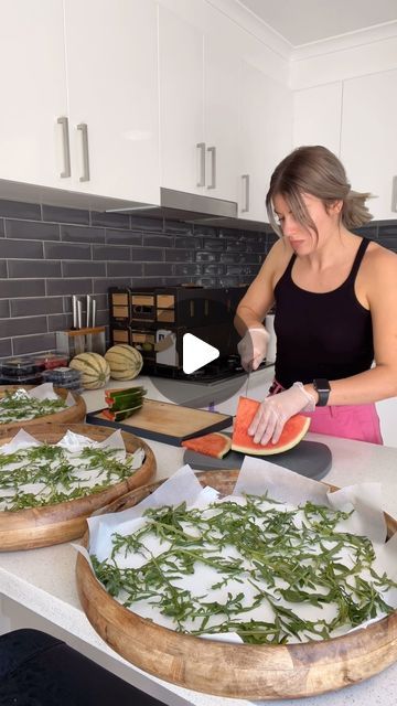 a woman cutting up slices of watermelon on top of a kitchen counter next to other pizzas