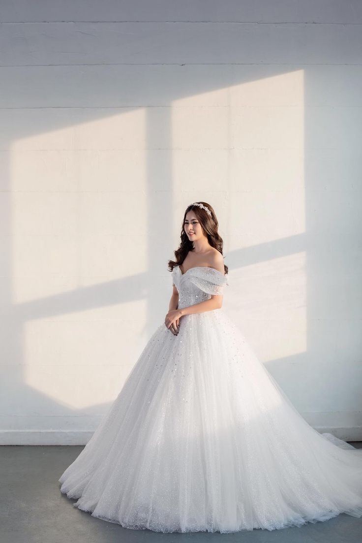 a woman in a white wedding dress standing against a wall with her hands on her hips