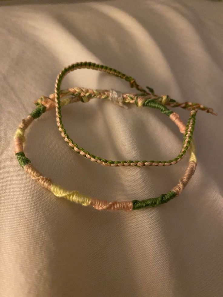 two braided bracelets sitting on top of a white cloth covered bedding area