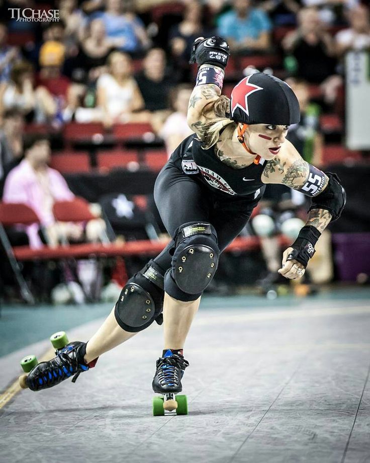 a woman riding a skateboard on top of a hard surface covered ground with spectators in the background