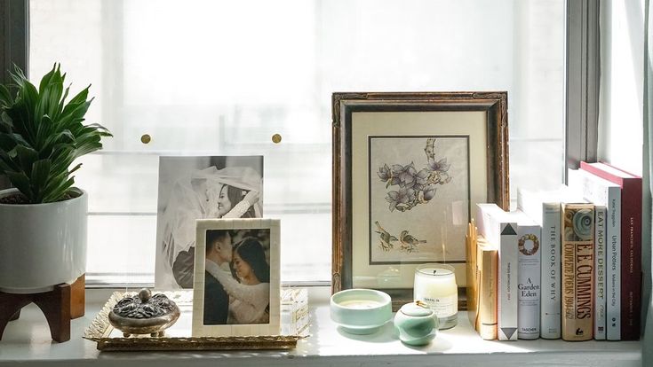 a window sill filled with books and pictures next to a potted plant on top of a table