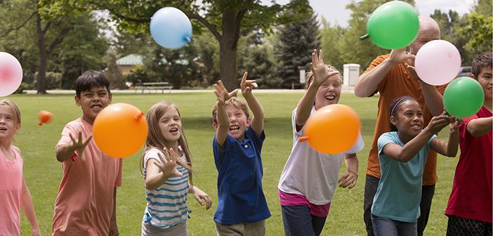 a group of young children holding balloons in the air while standing on top of a grass covered field