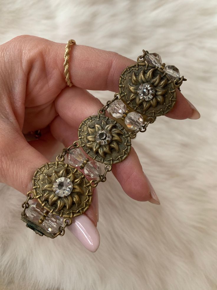 This Vintage 1930's Bead and Stamped Gold Tone Bracelet add romance and whimsy to any occasion. The metal is gold tone. The top of the metal is a flower shape, similar to a sunflower. The center of the flower is a zircon crystal adding pop and sparkle. In between the metal portions there are 2 crystal tone beads. The clasp of the bracelet even has a leaf embellishment. This bracelet is light-weight, flexible, and shows little signs of age. Length: 7.5 Inches Width: 1 inch Unless otherwise stated Antique Gold Bracelets For Vintage Events, Vintage Adjustable Gold Jewelry, Vintage Adjustable Jeweled Bracelets, Vintage Bracelet Jewelry For Vintage Events, Vintage Antique Gold Jeweled Jewelry, Antique Jeweled Metal Bracelets, Vintage Jeweled Gold Bracelets, Adjustable Vintage Jeweled Bracelets, Vintage Adjustable Gold Bracelets