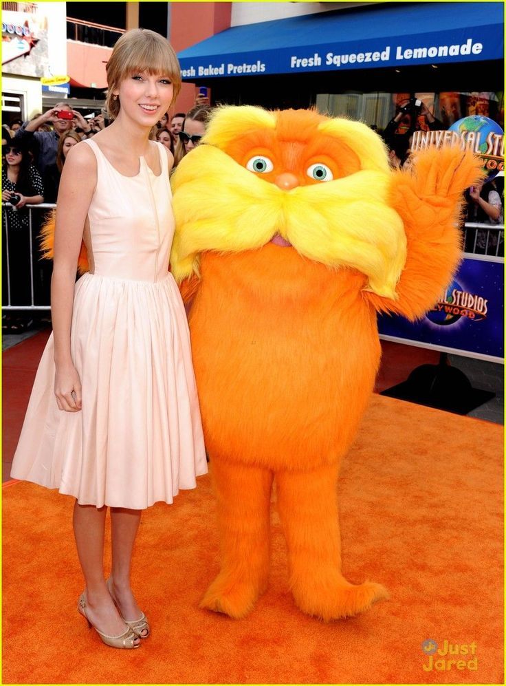 a woman in a white dress standing next to a large orange cat on an orange carpet