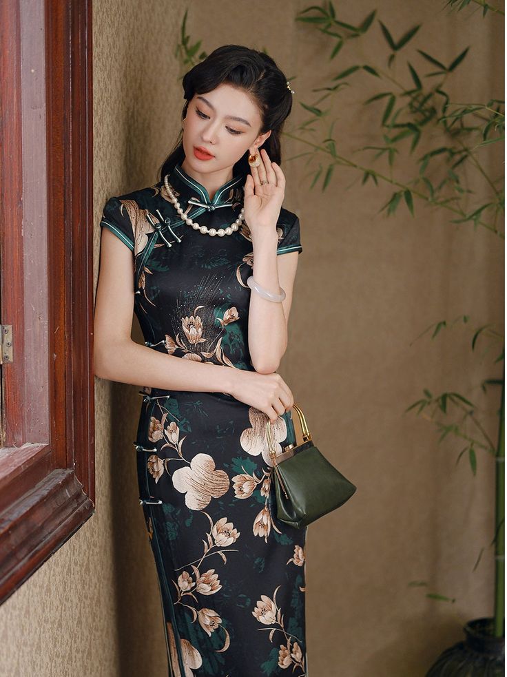 Step into elegance with this luxurious black silk qipao adorned with an exquisite floral design. The dress features a high Mandarin collar and traditional frog buttons, giving it a refined, authentic look. The rich green floral motif, interspersed with delicate cream and gold blossoms, adds a touch of nature-inspired beauty, making it perfect for formal occasions, evening events, or as a statement piece for special gatherings. Material: 90% Mulberry Silk, 10% Spandex Size Guide: Please note Asia Elegant Floral Print Cheongsam With Stand Collar, Elegant Black Cheongsam For Spring, Elegant Green Dress With Stand Collar, Traditional Black Dress With Floral Print, Elegant Fitted Cheongsam With Floral Print, Traditional Black Floral Print Dress, Traditional Fitted Floral Print Cheongsam, Traditional Fitted Floral Cheongsam, Green Elegant Cheongsam With Stand Collar