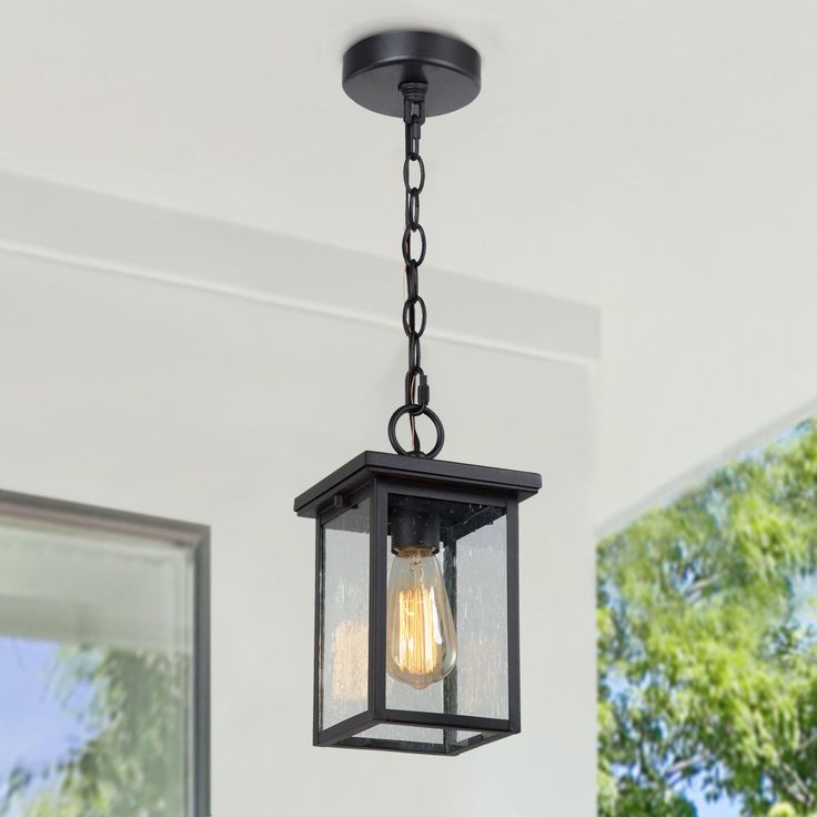 an outdoor light hanging from the ceiling in a room with white walls and green trees