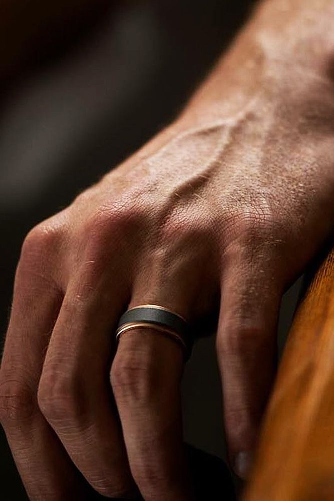 a man's hand with two wedding bands on it, resting on a wooden surface