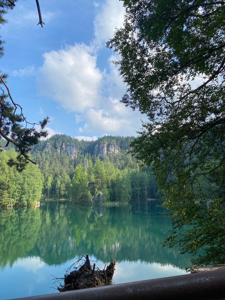 a lake surrounded by trees and mountains under a blue sky with clouds in the background