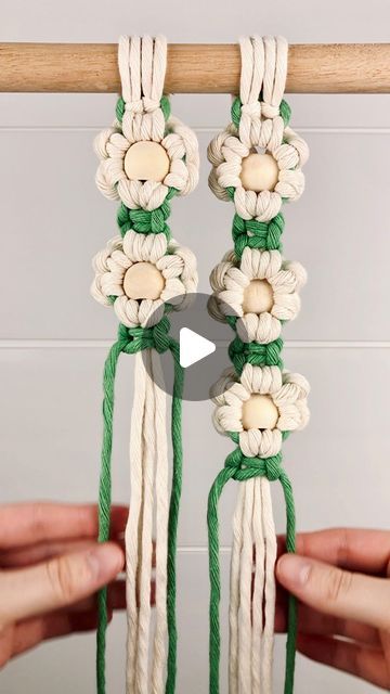 two hands are holding up some white and green macrame with flowers on them