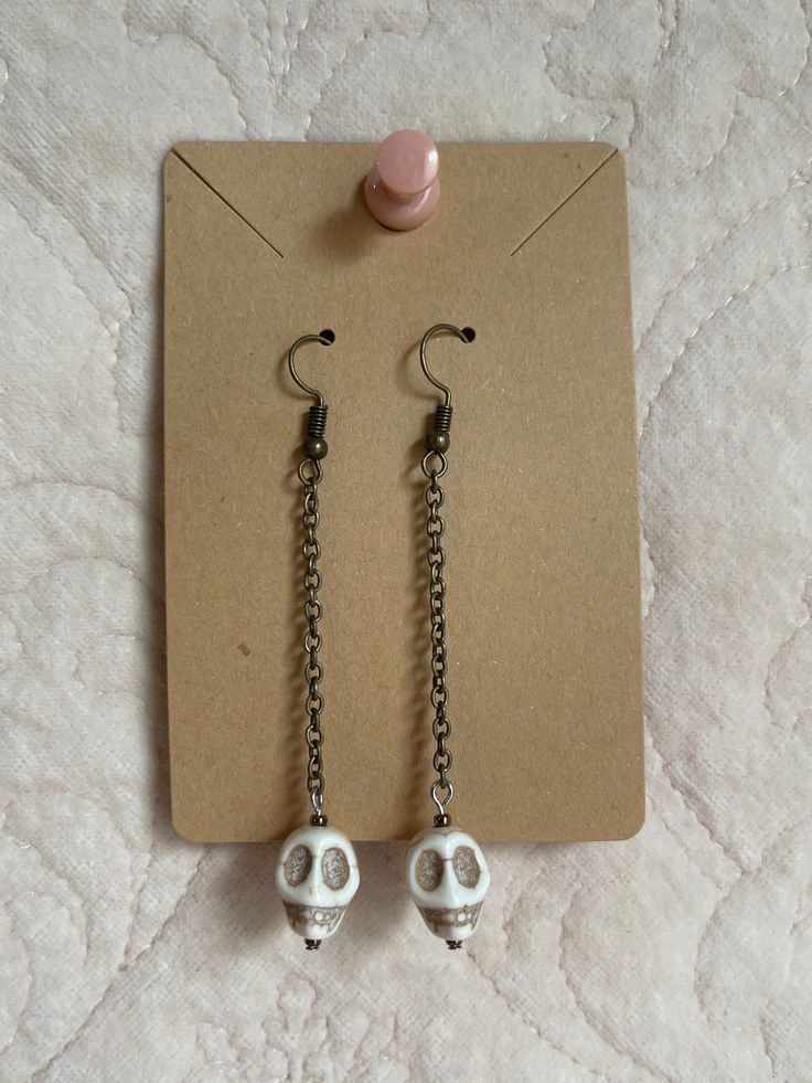 Handmade skull dangling earrings. I have seven available, all of them slightly vary in length from 2 3/4 inches - 3 inches. Skull beads are all unique with the line detail on the skull. Chain color is brass. Message me with any questions you might have!  Thanks for visiting my shop! Bone Color Dangle Earrings With Ear Wire, Nickel-free Bone Dangle Earrings, Nickel-free Bone-colored Dangle Earrings, Nickel Free Bone Color Dangle Earrings, Adjustable Gothic Skull Earrings, Skull-shaped Metal Earrings With Ear Wire, Metal Skull Earrings With Ear Wire, Nickel Free Metal Skull Earrings, Handmade Metal Skull Earrings