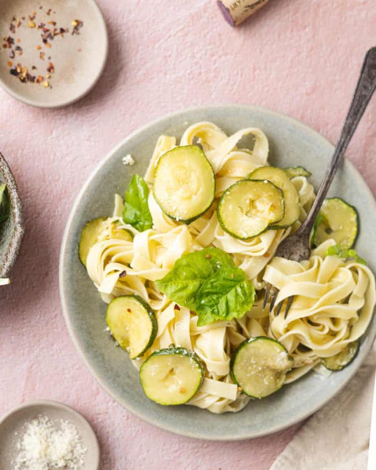 a bowl filled with pasta and cucumbers on top of a pink table cloth