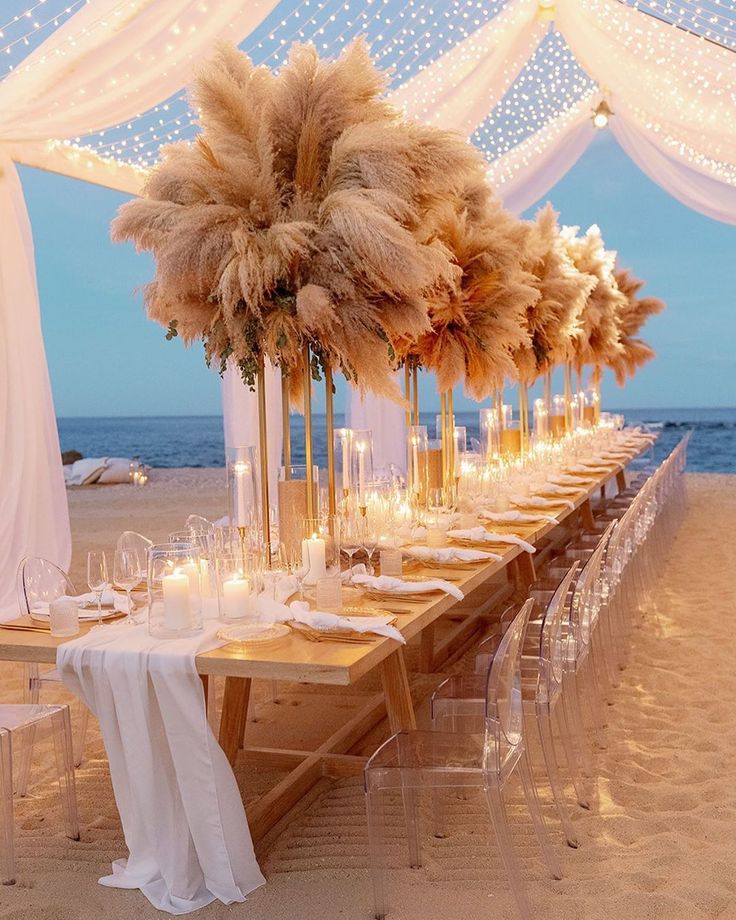 a long table set up on the beach with candles and pamolite centerpieces