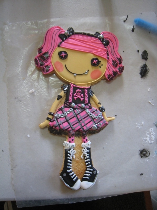 a cookie shaped like a girl with pink hair and black boots on top of a table