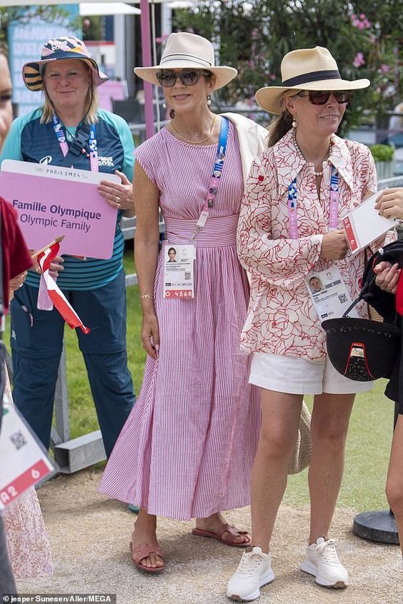 two women in dresses and hats standing next to each other at an outdoor sporting event