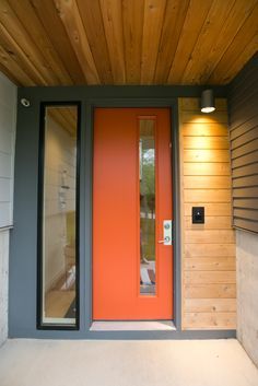 an orange front door is on the side of a house with wood paneled walls