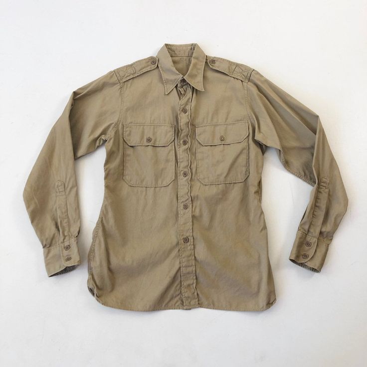 "1950's Marines khaki long sleeve shirt has a buttoned chest pockets, epaulettes, and a button front and cuff. Condition Structurally good. Has yellowish discoloration across the back, on both sleeves and around the front hem. Measurements Chest 40\" Waist 36\" Shoulder 15\" Sleeve length 25\" Length 27.5\" front, 30.5\" back. Best for a size small." Khaki Long Sleeve Shirt With Flap Pockets, Khaki Shirt With Spread Collar And Buttons, Khaki Shirt With Buttons And Spread Collar, Khaki Collared Shirt With Snap Buttons, Classic Khaki Shirt With Buttons, Military Style Long Sleeve Shirt With Buttons, Classic Khaki Shirt, Classic Long Sleeve Khaki Shirt, Khaki Military Collared Shirt