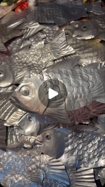 several metal fish on display in a pile with plastic wrap around them and one is looking up at the camera