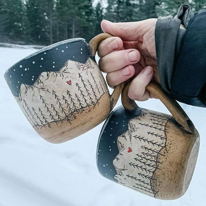 someone holding two mugs in the snow with trees in the backgroung