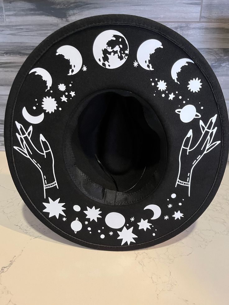 *due to printing there might be slight placement differences than pictured. A sturdy thick 100% polyester hat. I have applied moons and a cosmic theme in white. Get your witchy vibe on. It has adjuster inside. Size S/M 22.3 inch circumference Size M/L 22.8 inch circumference and 3.25 inch brim. Has inside adjuster. Black Brimmed Witchy Hat, Black Witchy Brimmed Hat, Black Witchy Hat With Curved Brim, Black Brimmed Witchy Costume Hat, Witchy Black Brimmed Costume Hat, Black Witchy Brimmed Costume Hat, Witchy Hat With Curved Brim, Black Wide Brim Costume Hat For Festivals, Black Fedora Halloween Costume Hat