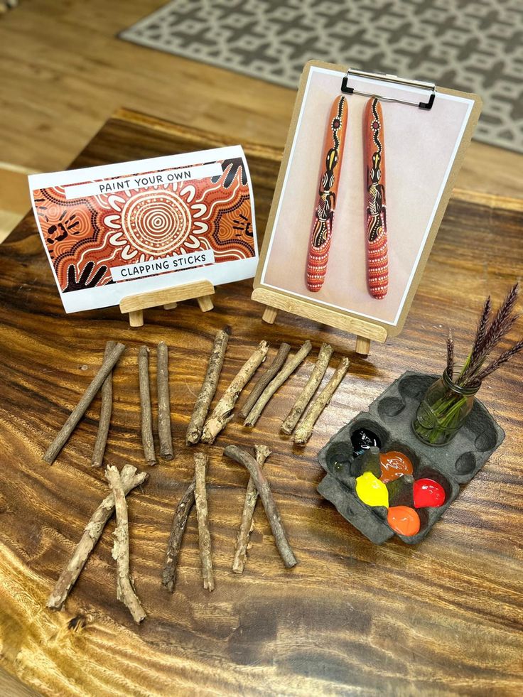 an assortment of crafting supplies including sticks, paint and paper on a wooden table