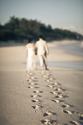 two people walking on the beach with footprints in the sand