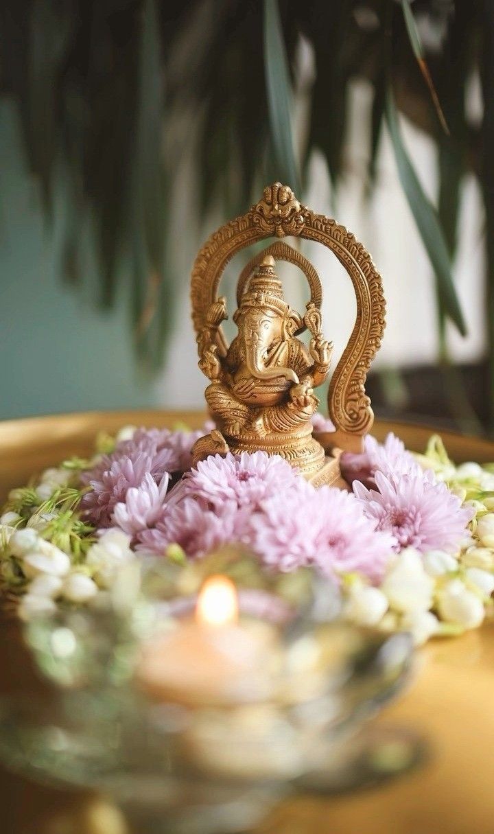 a small gold statue sitting on top of a table next to flowers and a candle