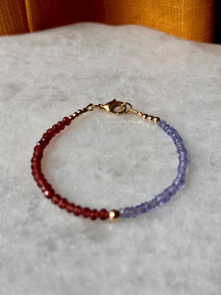 Elegant and dainty, this handmade bracelet features sparkling faceted 3mm Tanzanite and Garnet beads, showcasing a captivating interplay of deep reds and rich blues. Measuring about 7 inches in length, it is finished with a secure gold-filled lobster claw clasp, adding a touch of luxury to this exquisite piece Dainty Faceted Beaded Bracelets For Everyday Wear, Everyday Faceted Rondelle Bracelets, Dainty Faceted Beaded Bracelets, Faceted Rondelle Crystal Bracelet Gift, Dainty Round Beaded Bracelets With Faceted Beads, Faceted Rondelle Beaded Bracelets As Gift, Faceted Round Bead Bracelets For Gift, Faceted Bracelet Gift, Faceted Round Beads Bracelet For Gift