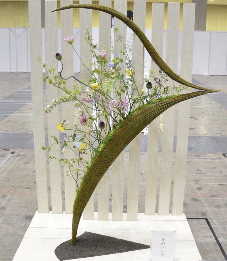 a vase with flowers on display in front of a white fence and wooden slats