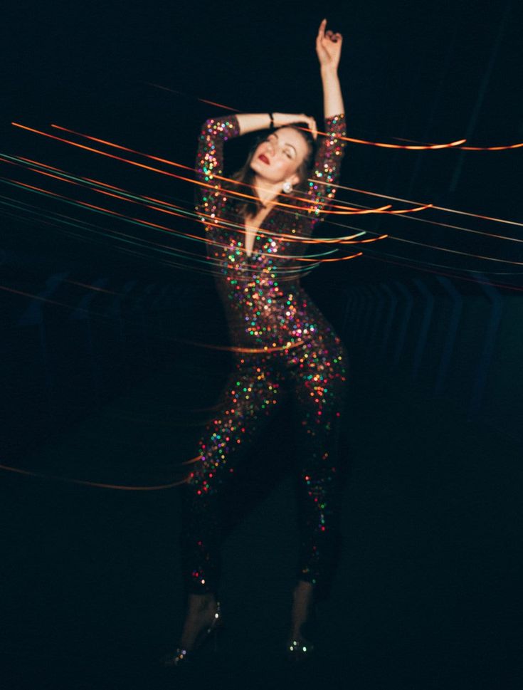 a woman is dancing in the dark with lights on her body and hands behind her head