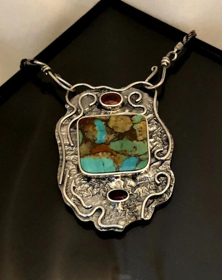 a silver and turquoise stone necklace sitting on top of a black table next to a white wall